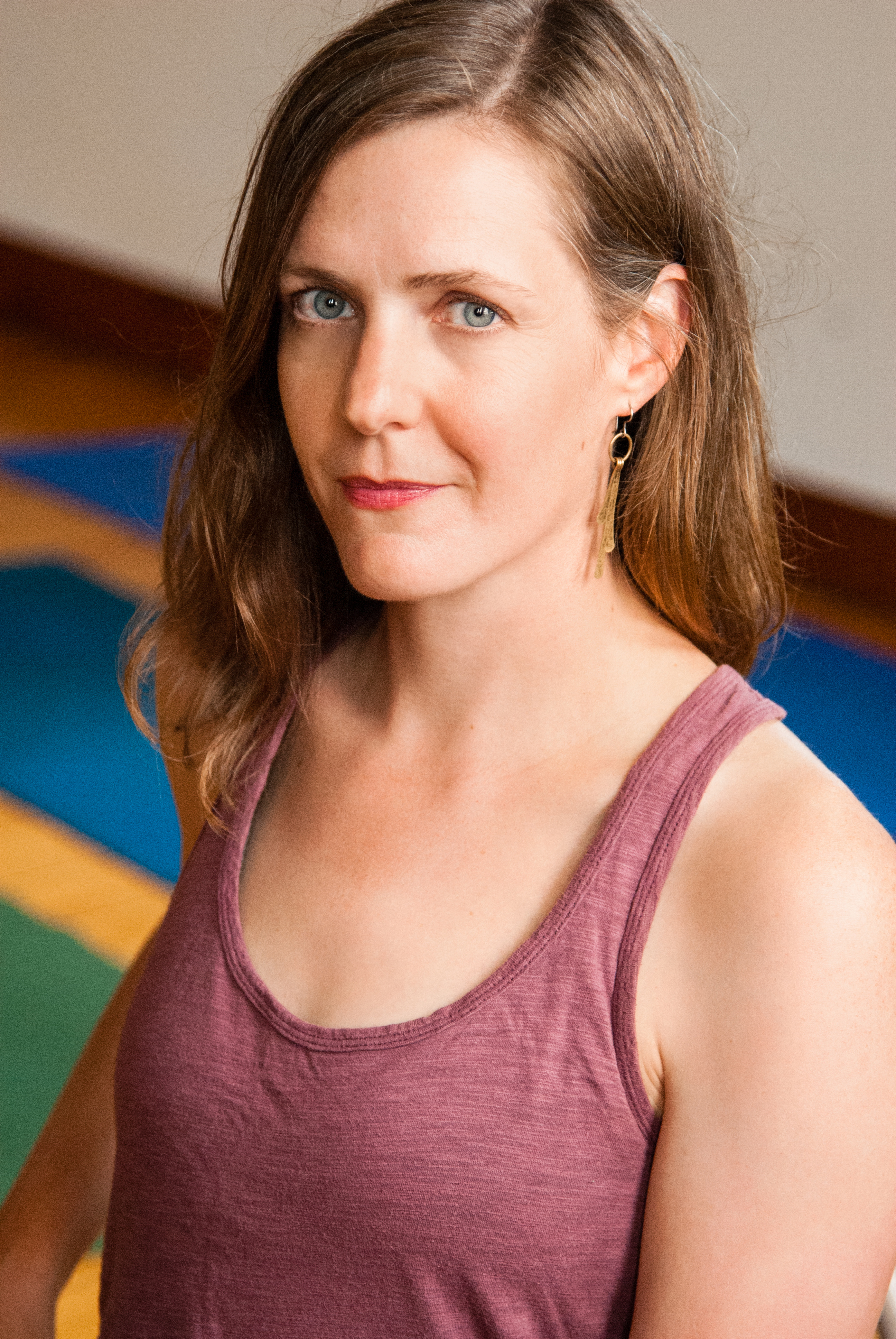 A picture of Erin Ehlers, a white woman in a pink tank top with blue yoga mats behind her.
